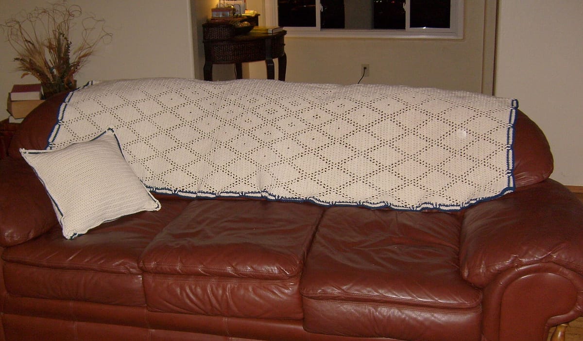 Filet crochet blanket in ecru with a blue edge on a sofa, an example of how to crochet a blanket