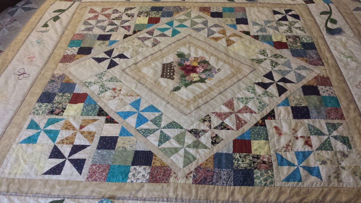 Handmade patchwork quilt with pinwheel blocks on a queen bed, an example of how to make a quilt